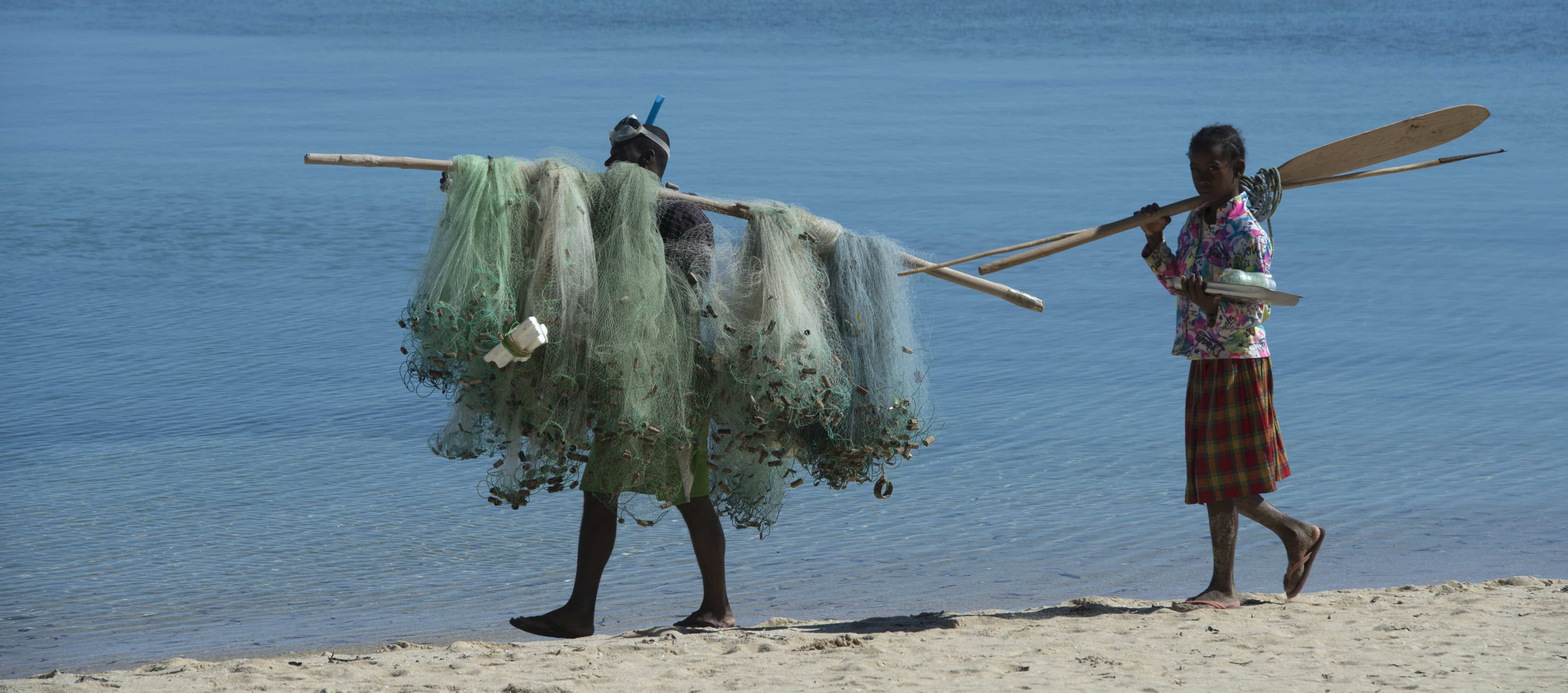 Madagascar - A fisherman carrying his nets and his daughter carrying the paddle and the spear along the beach on their way home at the end of the day.